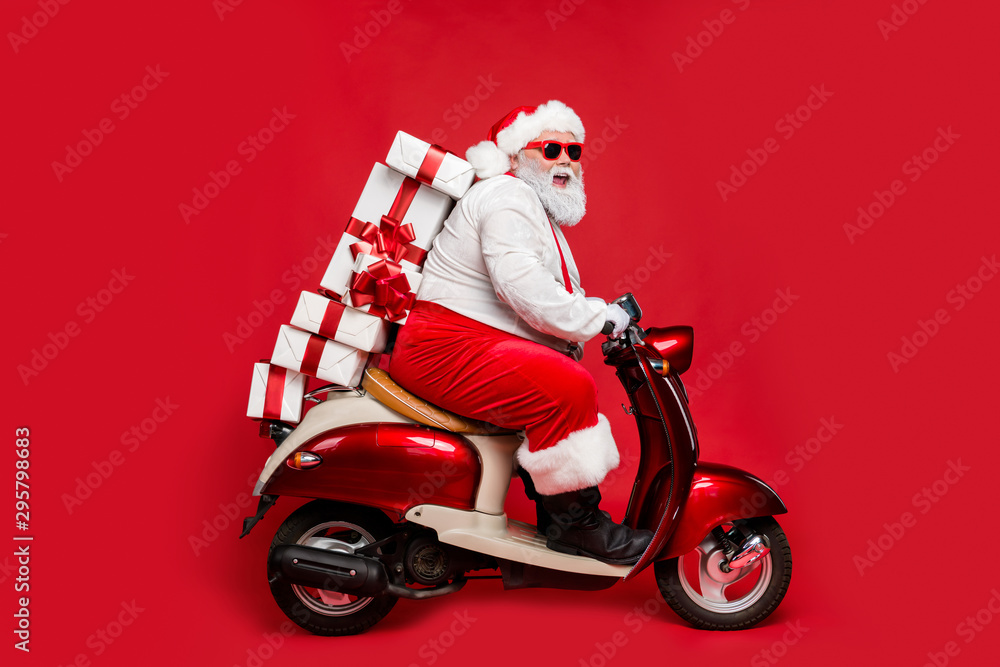Profile side view portrait of nice bearded cheerful cheery funny funky  Santa riding moped hurry up delivering pile stack winter purchases isolated  on bright vivid shine vibrant red color background Stock Photo |