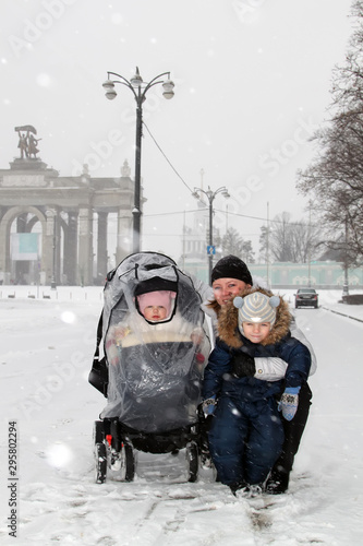 Young happy mother and her two adorable little kids having fun on winter day at city