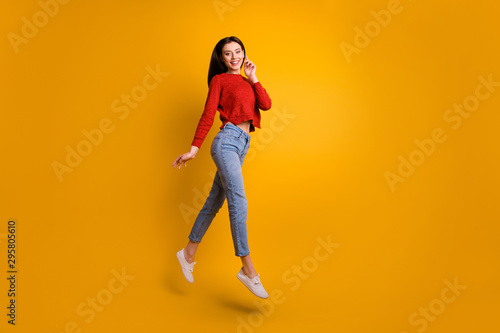 Full length photo of positive cheerful satisfied girl jump have free time with her friends go walk enjoy autumn holidays wear trend outfit isolated over yellow color background