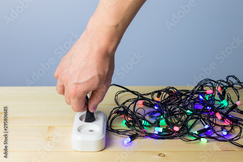 A man's hand plugged a Christmas garland into an electrical outlet, preparation for the holiday