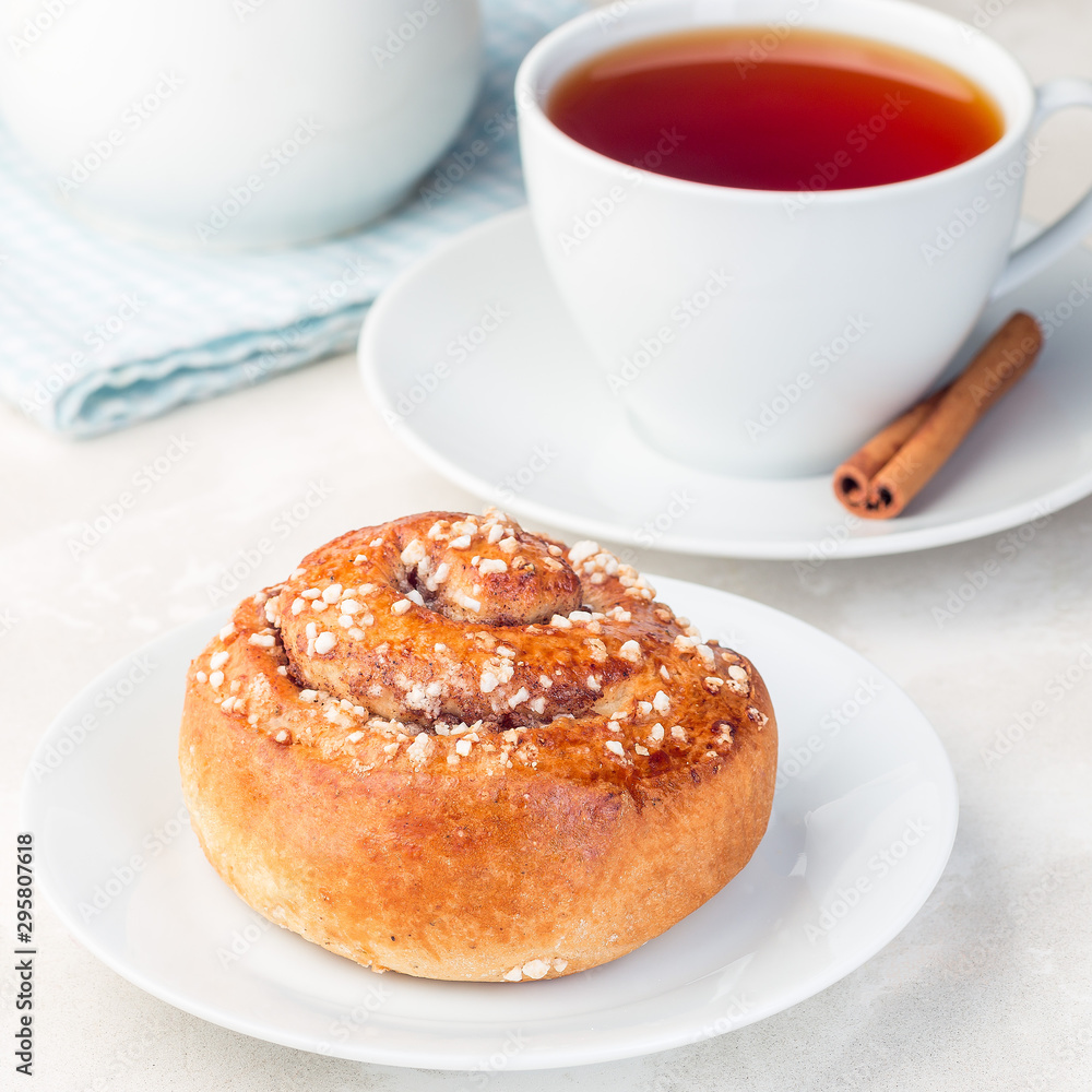 One cinnamon bun on a white plate, served with a cup of red tea, square format, closeup One cinnamon bun on a white plate, served with a cup of red tea, square format, closeup