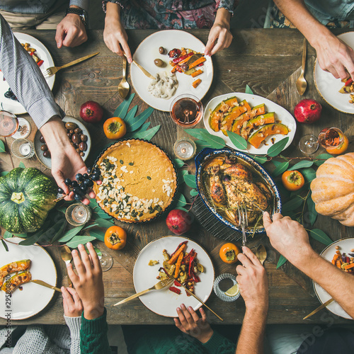 Thanksgiving, Friendsgiving holiday celebration. Flat-lay of friends eating meals at Thanksgiving Day table with turkey, pumpkin pie, roasted vegetables, fruit, rose wine, top view, square crop
