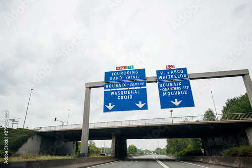 Driver POV personal perspective at the highway autoroute sign with cities names - Roubaix, Wasquehal, Croix, Mouvaux, ASCQ Watterlos, Gand traveling in French city