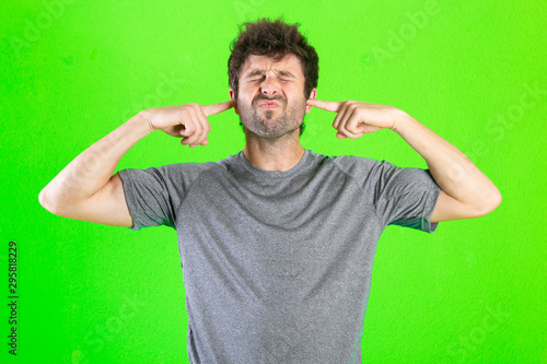 Young crazy man covering his ears, noise concept over green background