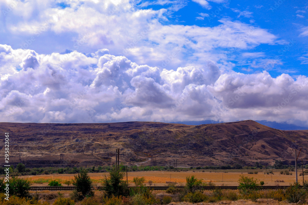 Fototapeta premium Settlement in valley, mountains and white clouds in the blue sky.