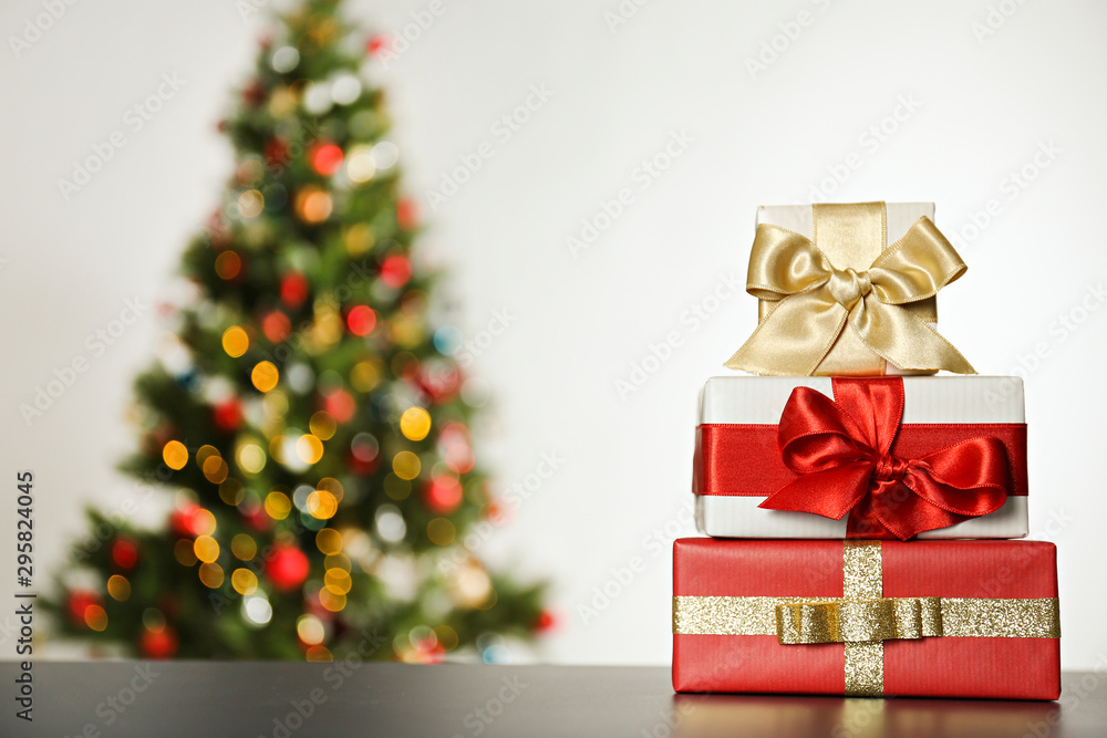 Festive composition with stack of many different presents in colorful wrapping paper on foreground and blurry decorated Christmas spruce tree on background. Close up, copy space.