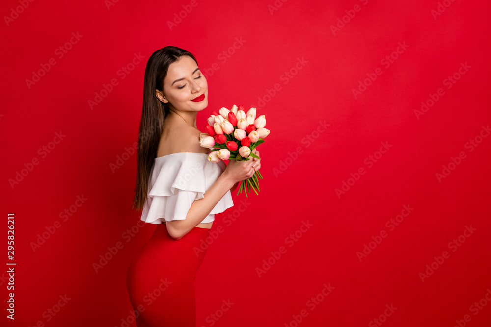 Portrait of cute youth enjoying flowers aroma closing eyes wear white off-shoulders isolated over red background Portrait of cute youth enjoying flowers aroma closing eyes wear white off-shoulders isolated over red background