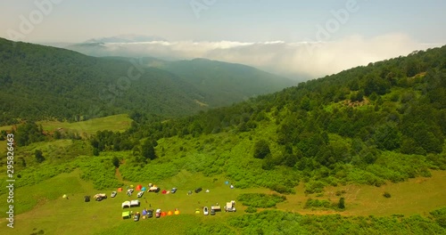 A bird eye view shot of tourists camp middle in green nature A few people attending a camp and suv and 4wd car and tents middle in green landscape over high mountain and extended green nature