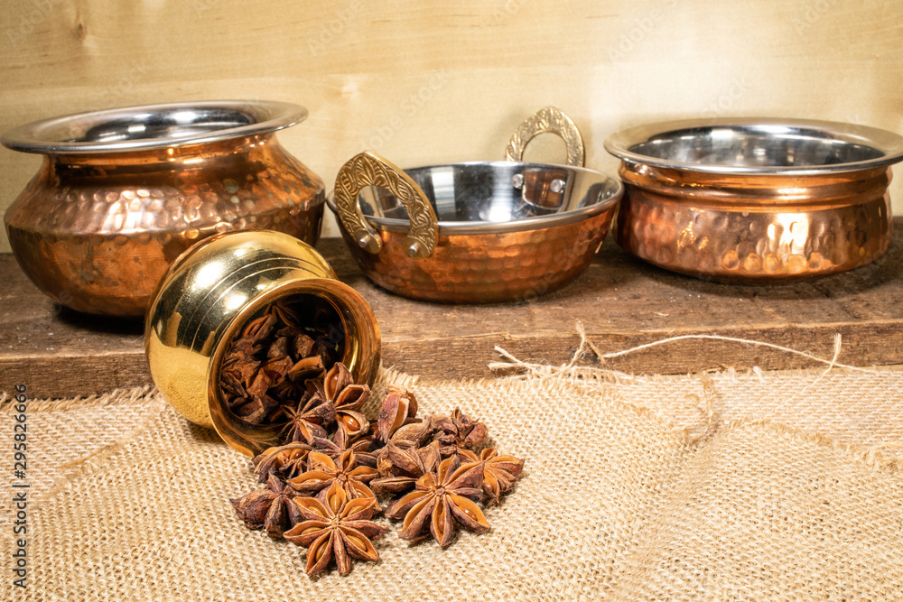Aromatic spice Star anise pouring from small brass copper pot jute textile wooden background Aromatic spice Star anise pouring from small brass copper pot jute textile wooden background