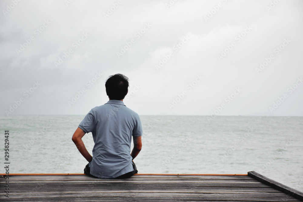 A lone man sitting on the wooden with sea vtew - obrazy, fototapety, plakaty 