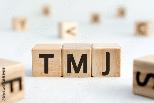 TMJ - acronym from wooden blocks with letters, abbreviation TMJ temporomandibular joint syndrome, TMD Temporomandibular disorder concept, random letters around, white  background photo