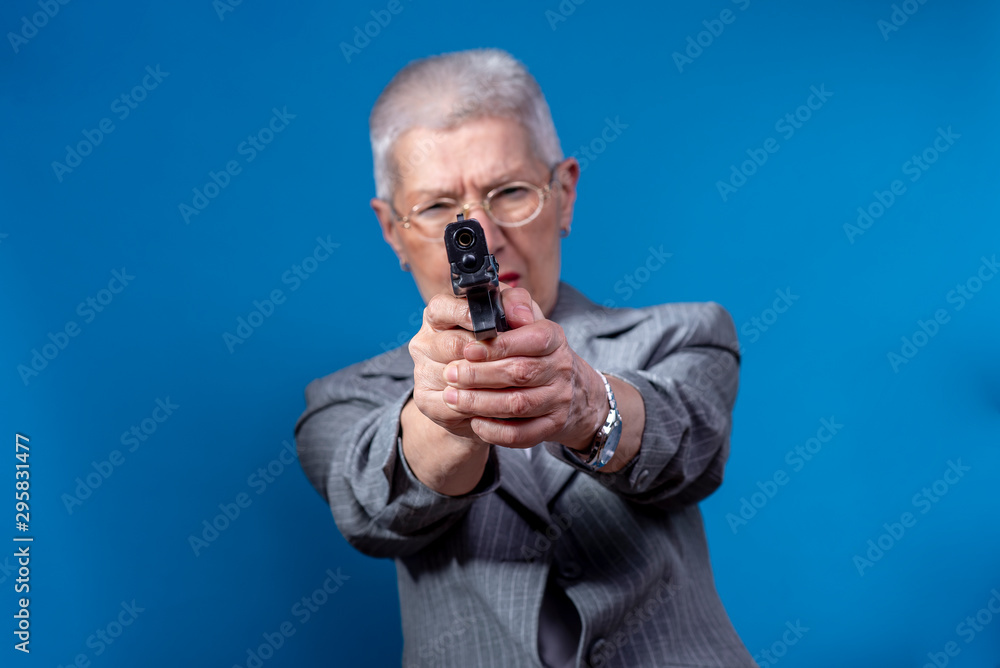 Old business lady aiming with her weapon, looking angry Old business lady aiming with her weapon, looking angry