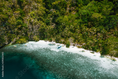 Aerial drone view of a secluded deserted tropical beach with lonely tourist boat surrounded by rainforest jungle. Cadlao Island  El Nido  Palawan