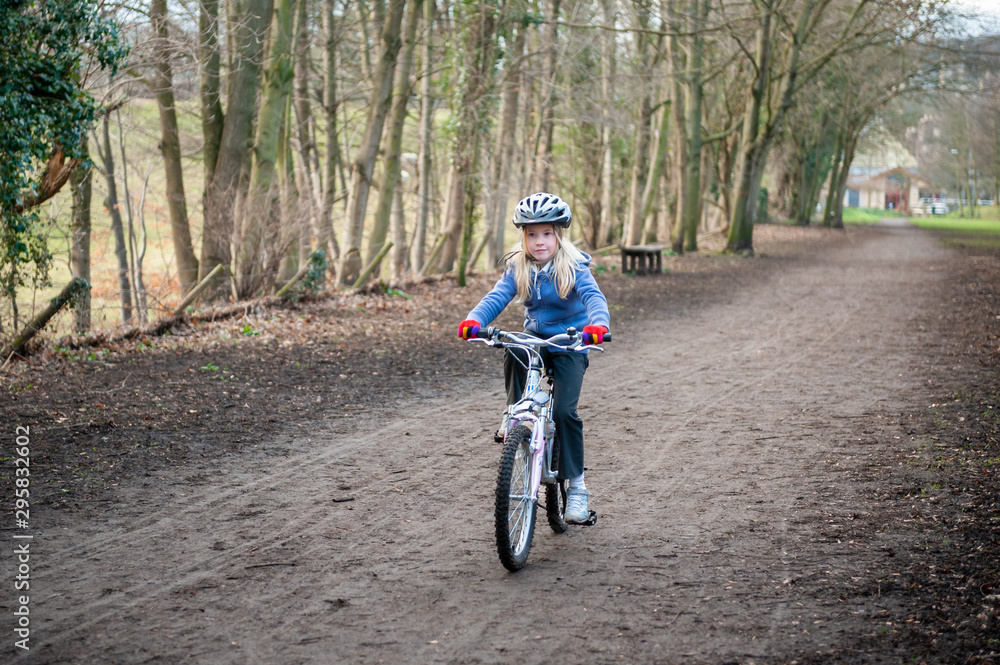 Young blonde girl riding bike along country path