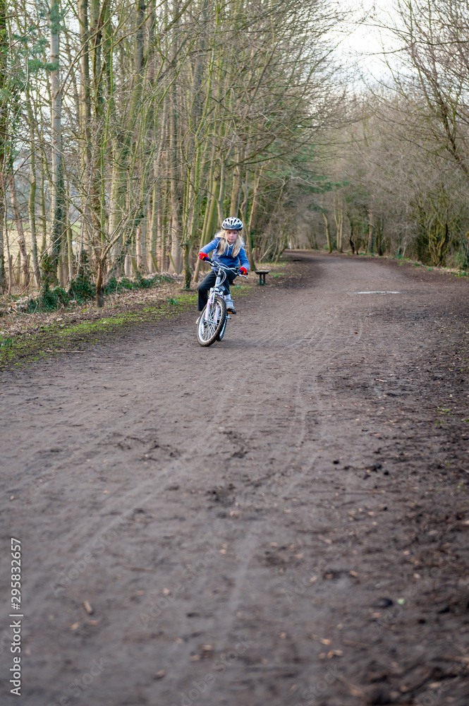 Young girl riding bike towards camera along country path. Vertical shot with copy space