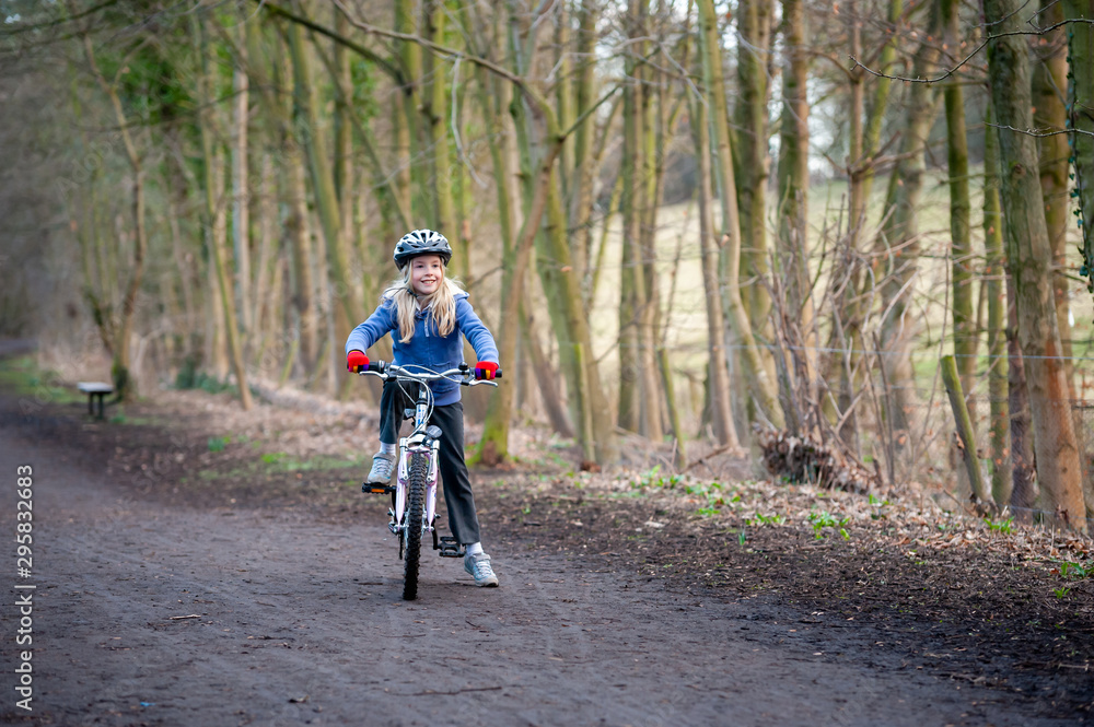 Smiling, happy young blonde girl paused on her bike on a country path