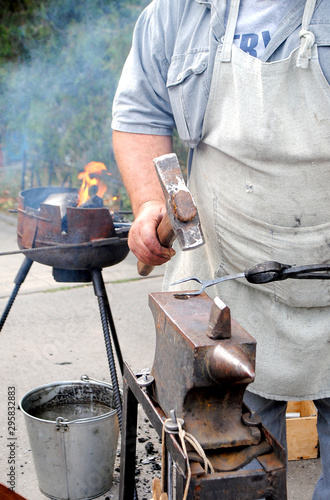 Blacksmith. Forging a medieval fork on an anvil. A blacksmith forges outdoors next to a brazier to heat the metal.