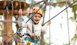 Little girl in helmet climbs ropes in adventure park outdoors. Extreme sport, active leisure on nature.