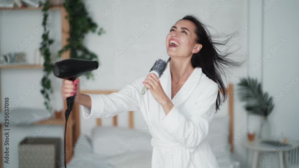 Young woman in white bathrobe dances, sings and dries hair with hairdryer Young woman in white bathrobe dances, sings and dries hair with hairdryer