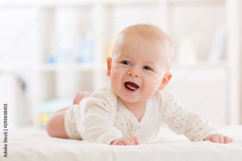 Baby boy wearing white clothes in sunny nursery room. Newborn child relaxing in bed. Baby boy wearing white clothes in sunny nursery room. Newborn child relaxing in bed.