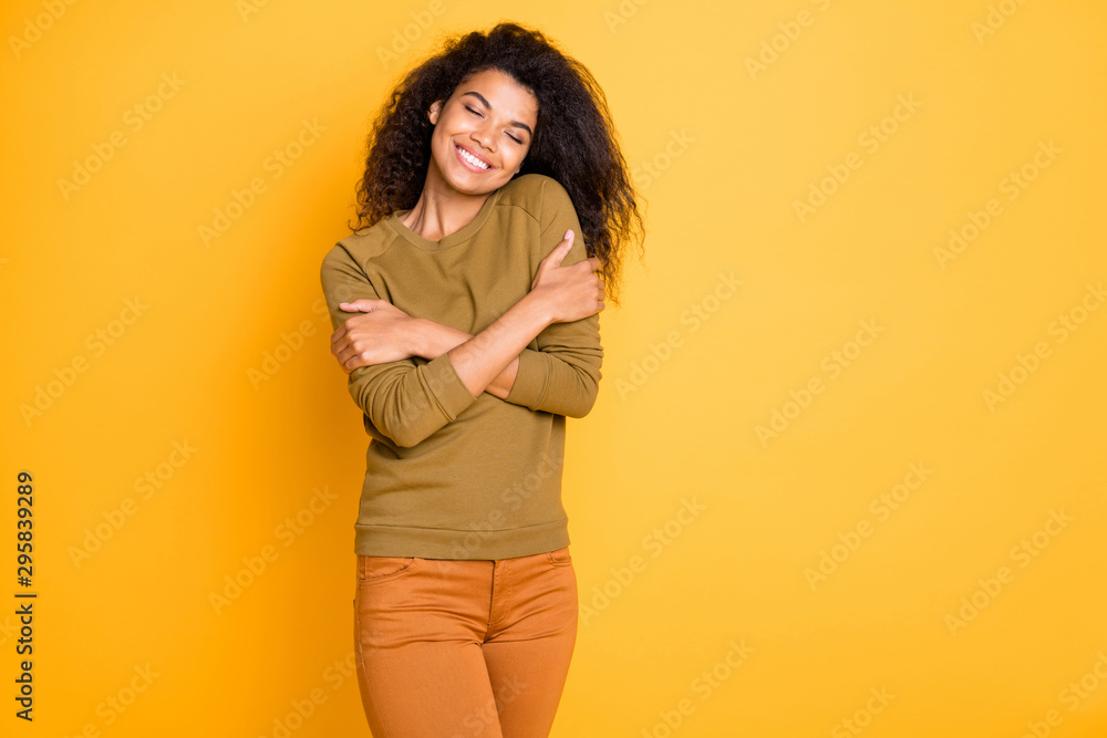 Photo of cheerful toothy beaming cute nice charming attractive black woman wearing orange pants trousers enjoying her newly bought sweater isolated over vivid color background