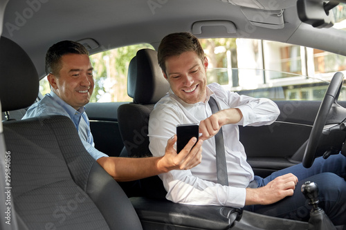 transportation, taxi and technology concept - middle aged male passenger on back seat showing his smartphone to car driver