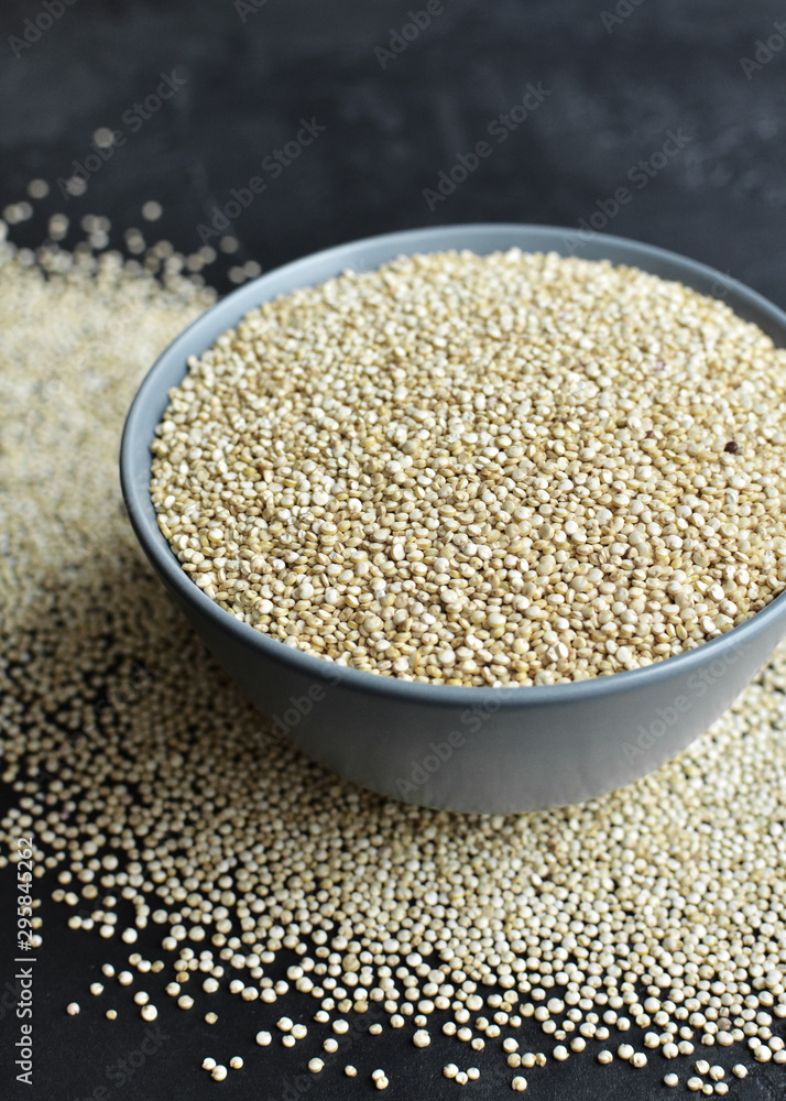 Dry organic quinoa seeds in ceramic bowl on dark concrete background Dry organic quinoa seeds in ceramic bowl on dark concrete background