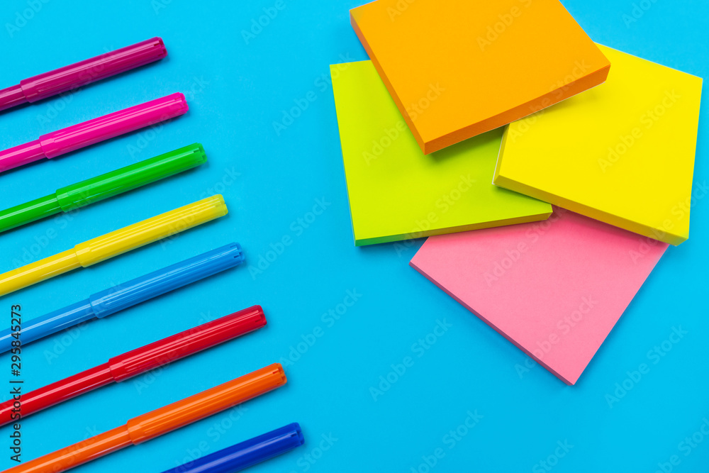 Photo of colorful bright felt-tip pens lying in the left corner on a blue background next to which is a set of yellow, orange, pink, green colors. Close-up. Stationery. Photo of colorful bright felt-tip pens lying in the left corner on a blue background next to which is a set of yellow, orange, pink, green colors. Close-up. Stationery.