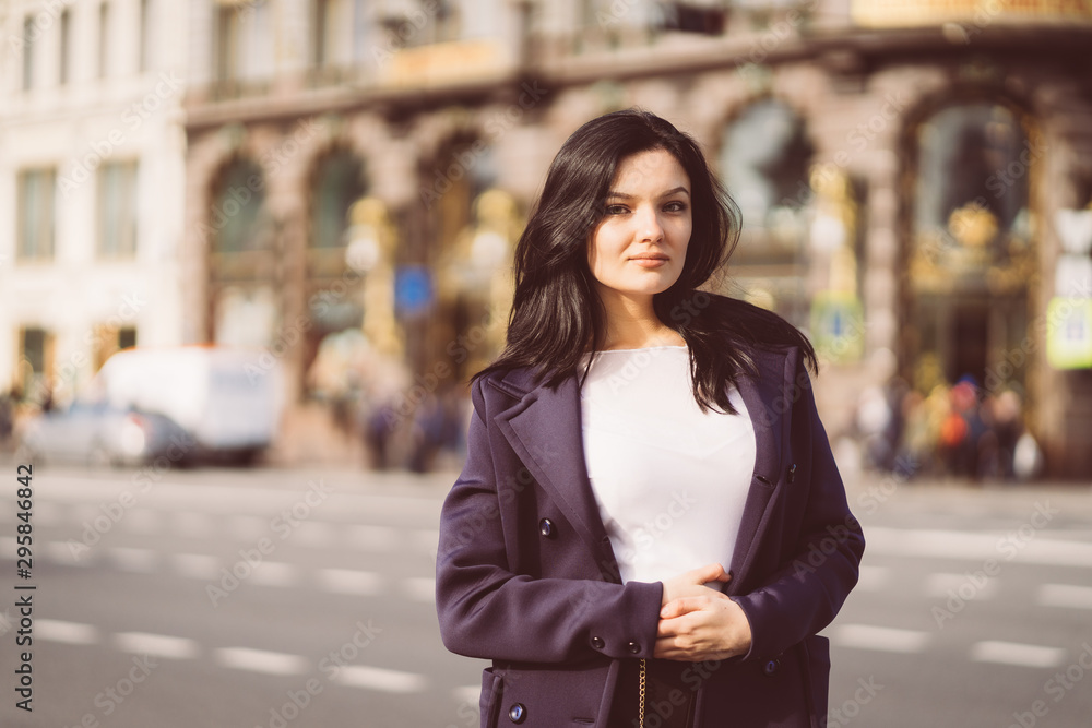 Fototapeta premium Portrait f beautiful intelligent brunette who walks down street of Saint-Petersburg in city center. Charming thoughtful woman with long dark hair wanders alone, immersed in thoughts