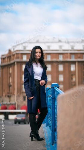 Charming thoughtful fashionably dressed woman with long dark hair travels through Europe, standing in city center of St. Petersburg. A beautiful girl wanders alone through autumn streets