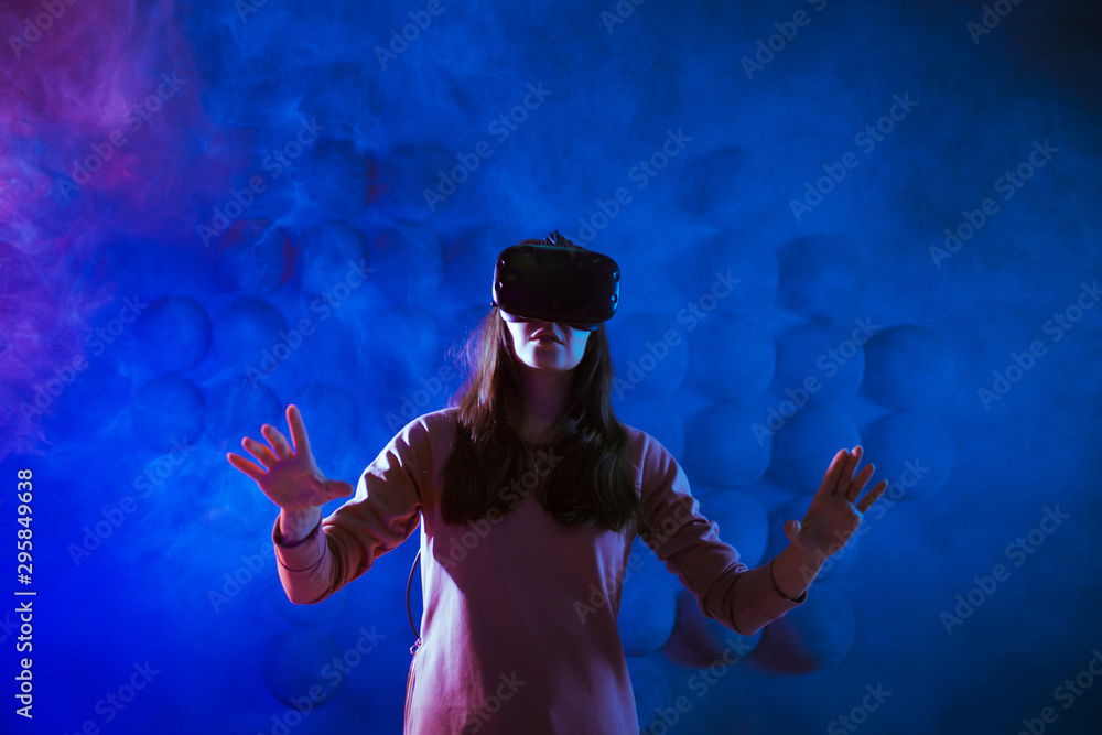 Journey begins. Amazed young woman touching air during the VR experience against neon and smoke futuristic background.