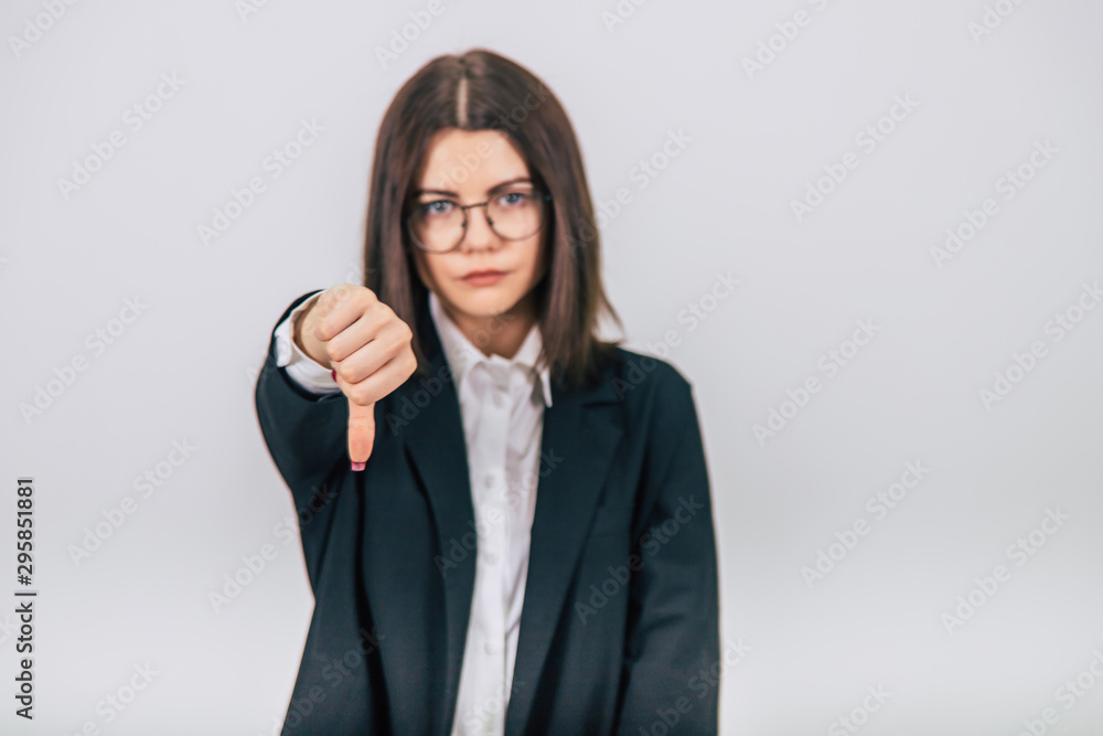 Blurred lovely young businesswoman in black suit standing, giving thumbs down, showing her dislike. Focus on the gesture. Blurred lovely young businesswoman in black suit standing, giving thumbs down, showing her dislike. Focus on the gesture.