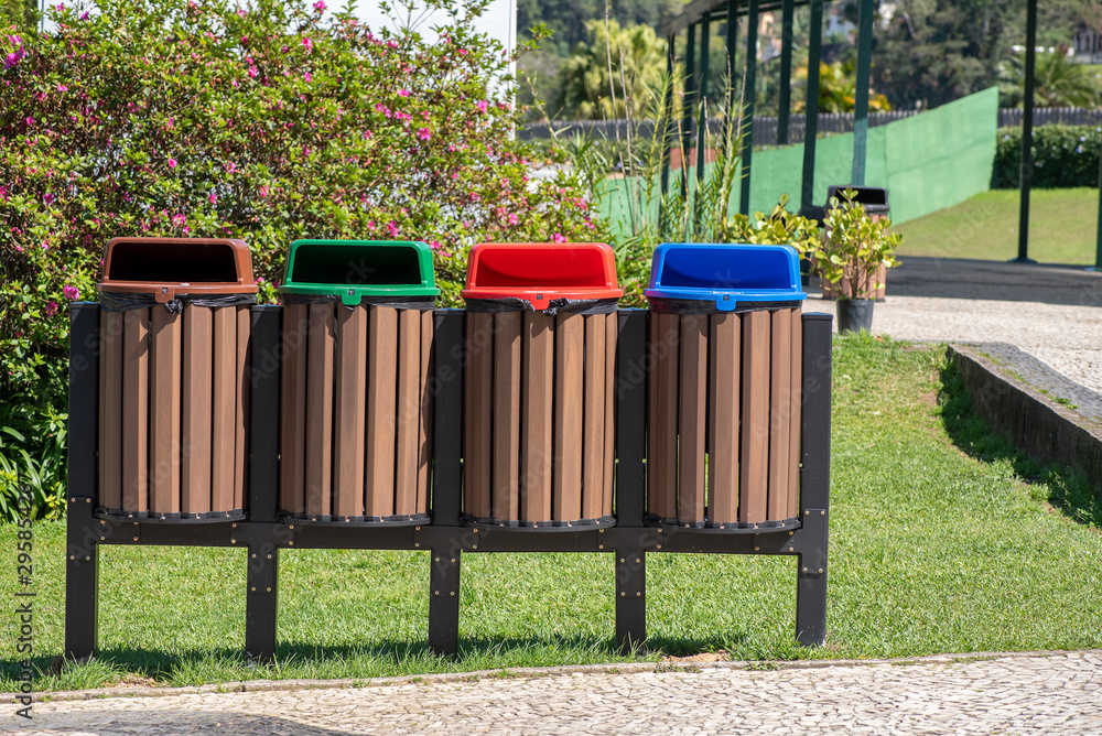 Four recycling bins at a park, colorful, each color signifying a type of recyclable item Four recycling bins at a park, colorful, each color signifying a type of recyclable item