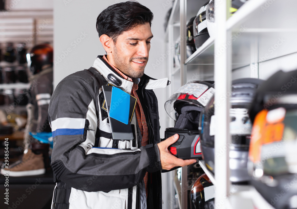 Male customer is choosing modern helmet near shelves