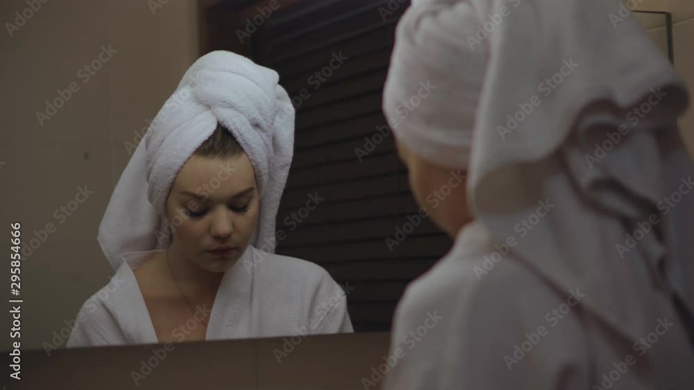 A Young Girl Smokes a Cigarette in front of the Mirror in the Shower. Hair wrapped in a white Towel. Luxurious Woman in the Bathroom at the Hotel on Vacation. A Young Girl Smokes a Cigarette in front of the Mirror in the Shower. Hair wrapped in a white Towel. Luxurious Woman in the Bathroom at the Hotel on Vacation.