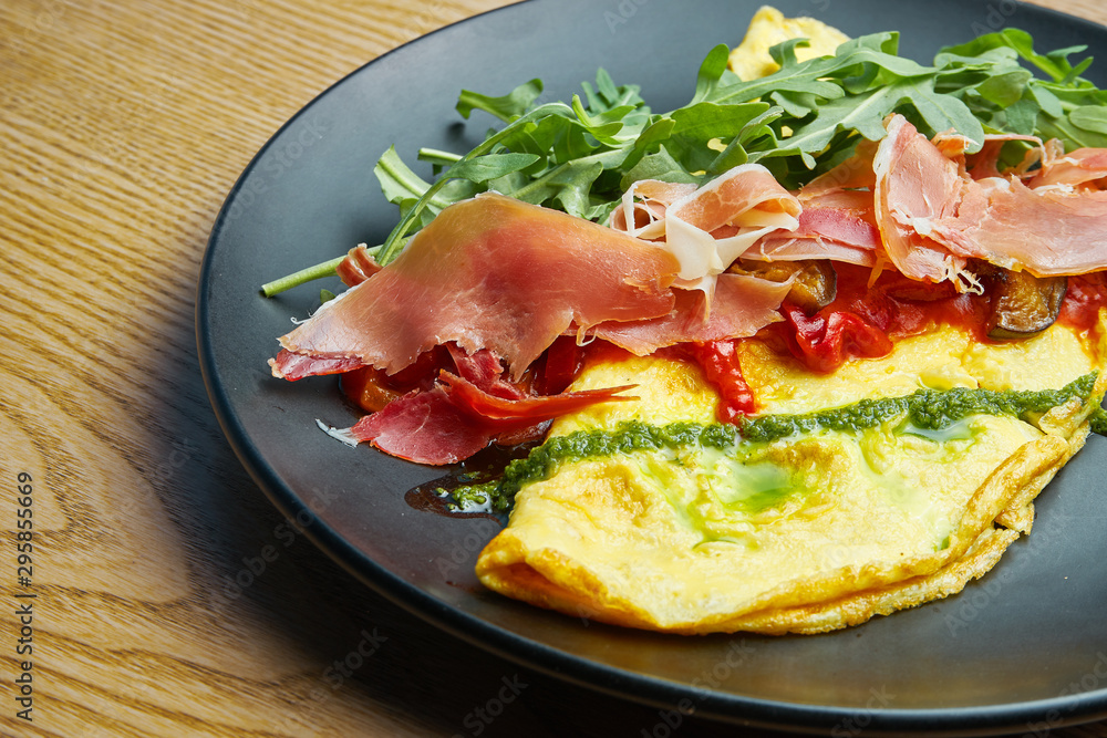 Frittata with prosciutto, pesto sauce, arugula and bell pepper on black plate. Tasty and healthy lunch. Omelette