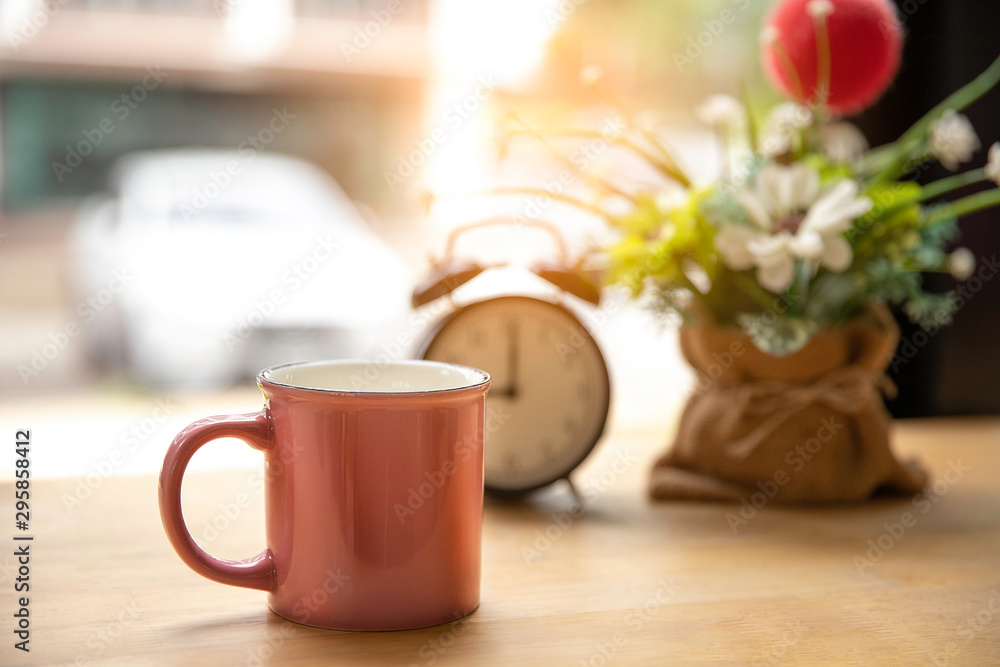 morning coffee in a pink cup with blurred clock and flowers on wooden table in coffee shop morning coffee in a pink cup with blurred clock and flowers on wooden table in coffee shop