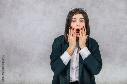 Fotografie Scared businesslady with glasses on the forehead, raising her hands, covering mouth, looking with eyes widely opened