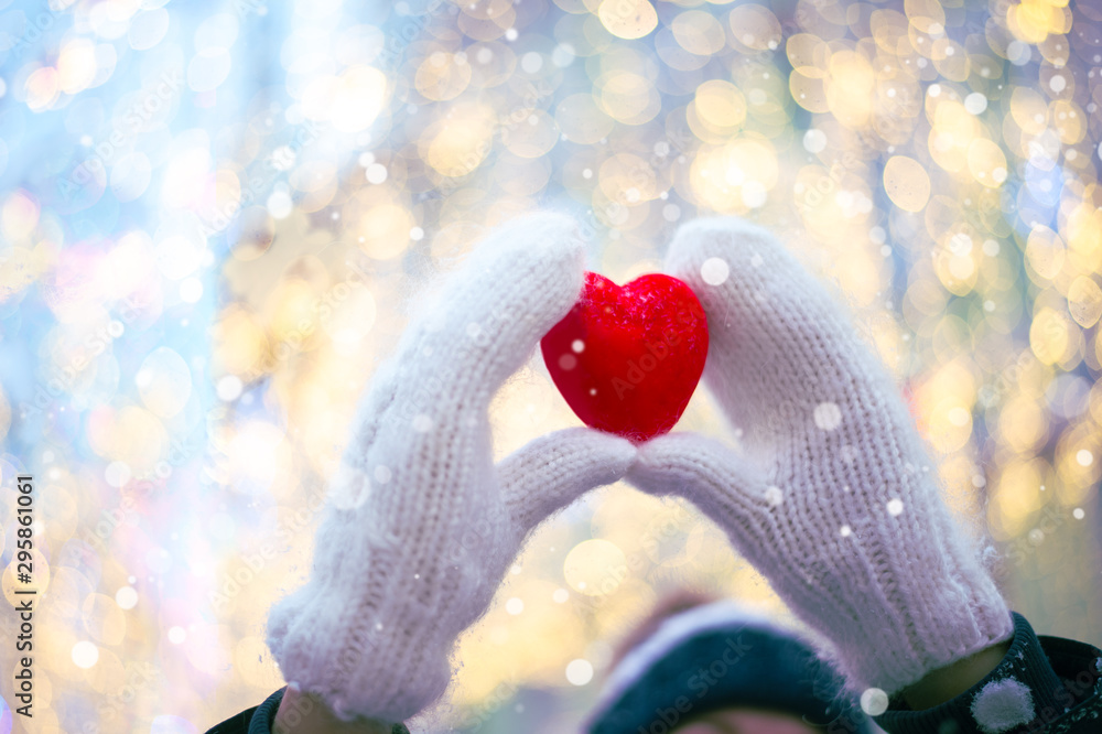 Woman hands in white knitted mittens with a red heart on a snow background. - obrazy, fototapety, plakaty 