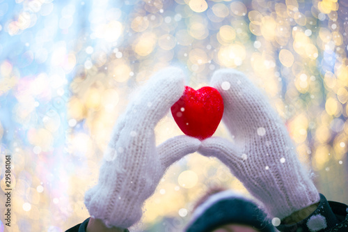 Woman hands in white knitted mittens with a red heart on a snow background.