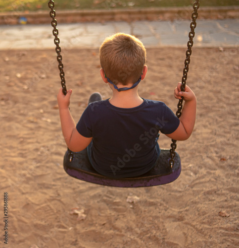 Blond boy with glasses swinging at sunset on a park swing photo