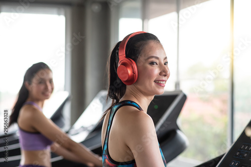 Side View Of Smiling Young Woman Wearing Red Headphones While Exercising On Treadmill In Gym