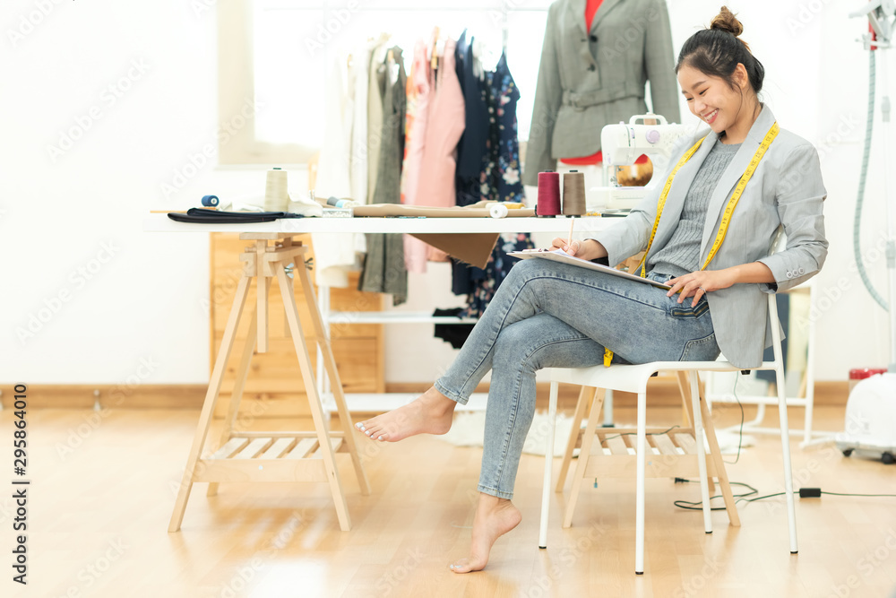 Asian young women fashion designer  working on her designer in the showroom,  Lifestyle Stylish tailor taking measurements on mannequin in studio.  Business small Concept