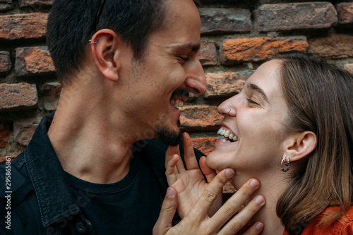 Couple laughing and stroking each other in front of a brick wall. photo