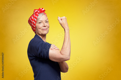 Senior rosie riveter concept: self-confident elderly woman with clenched fist rolling up her sleeve, copy space photo