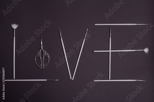 white brushes and beautiful openwork scissors for nail design on black background in the shape of the word love © ViRusian