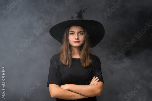 Girl with witch costume for halloween parties over isolated dark background keeping arms crossed © luismolinero