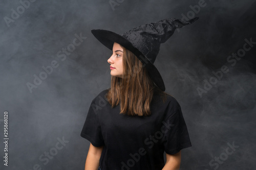 Girl with witch costume for halloween parties over isolated dark background looking side