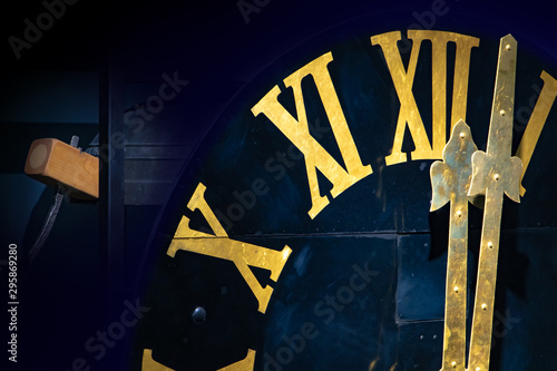 The clock with gilded Roman numerals shows twelve hours. The midnight on tower clock. Clock mechanism with hammer and the bells.