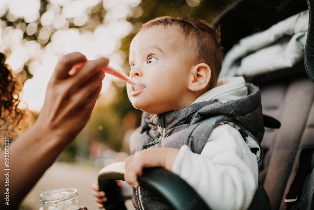 1 year old baby eating yogurt in stroller in city park 1 year old baby eating yogurt in stroller in city park